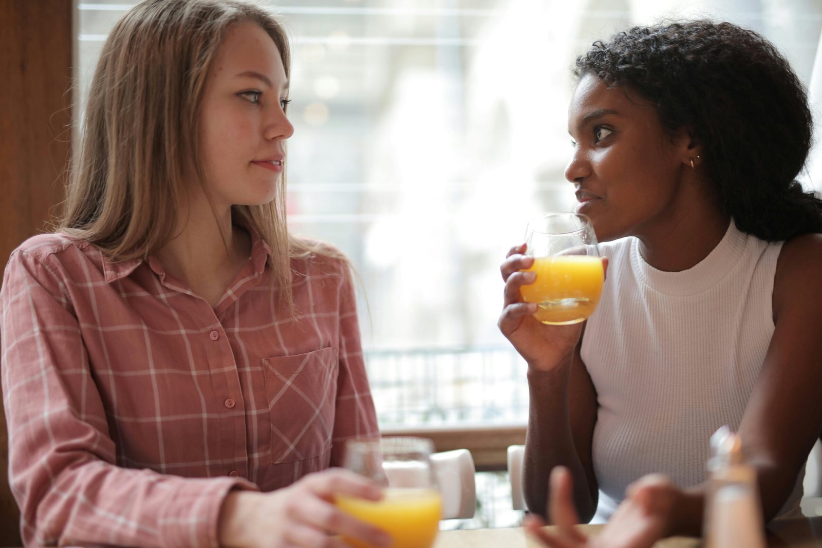 Two women enjoying a casual conversation while drinking orange juice in a café.